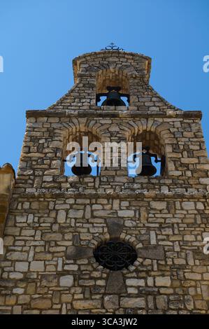 Una vista di uno storico campanile in pietra con archi e campane, che mostra l'artigianato dettagliato contro un cielo blu vivace, evocando rusti Foto Stock