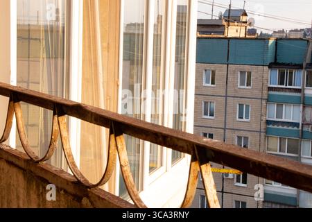 Vista da un balcone con ringhiere arrugginite sulle finestre di un edificio a pannelli adiacenti a più piani in Ucraina in estate al tramonto Foto Stock