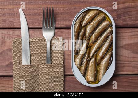 Barattolo di spratti, sardine con coltello e forchetta sul tavolo di legno. Vista dall'alto. Foto Stock