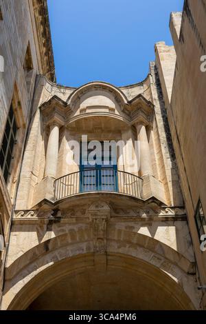 Old Theatre Street, con la passerella ad arco chiusa e il balcone della Biblioteca Nazionale, la Valletta, Malta. Foto Stock