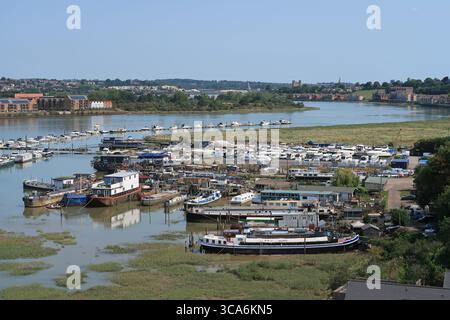 Case galleggianti e cantiere sul fiume Medway vicino a Rochester, Kent, Regno Unito. Vista a valle dal ponte dell'autostrada m2. Rochester Castle all'orizzonte. Foto Stock