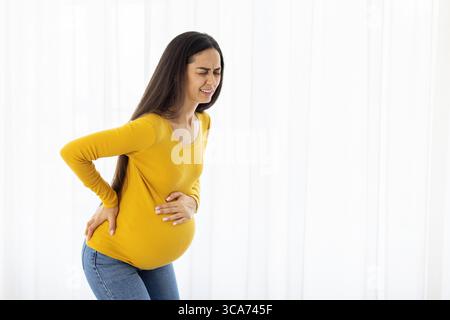 Donna incinta con mal di schiena visibile che tiene la pancia e la parte inferiore della schiena Foto Stock