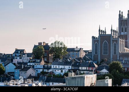 25 luglio 2025 Cork, Irlanda, Un aereo vola sopra una vivace città con una chiesa sullo sfondo Foto Stock