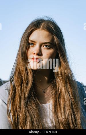 Una giovane donna con lunghi capelli marroni e occhi blu guarda la macchina fotografica Foto Stock