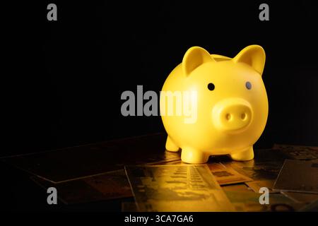 Il salvadanaio giallo siede sulle banconote in euro sparse, simboleggiando il risparmio finanziario e la stabilità economica. Ideale per temi legati al budget, al denaro Foto Stock
