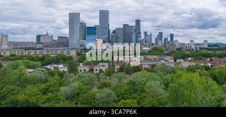 Lo skyline di Canary Wharf si vede da ovest, sorgendo dietro alberi e basse case Foto Stock