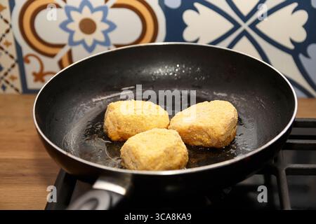 Una padella graffiata con deliziose cotolette semilavorate, che simboleggiano la preparazione rapida e semplice del cibo in una cucina affollata. Foto Stock