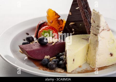 squisito dessert placcato con ricca torta al cioccolato, cremosi dolcetti surgelati, pera marinata e frutti di bosco freschi Foto Stock