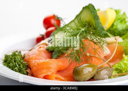 piatto salutare di salmone affumicato con cetriolo, pomodori, salsa ed erbe fresche su un piatto bianco, una foto da studio di un pasto gourmet Foto Stock
