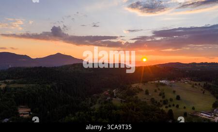 Una vista grandangolare del tramonto che illumina un paesaggio di montagna a strati con valli boscose e paesaggi rurali Foto Stock