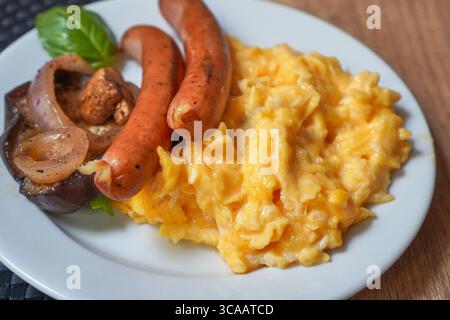 Salsicce grigliate servite con uova strapazzate, guarnite con verdure e pomodoro. Foto Stock