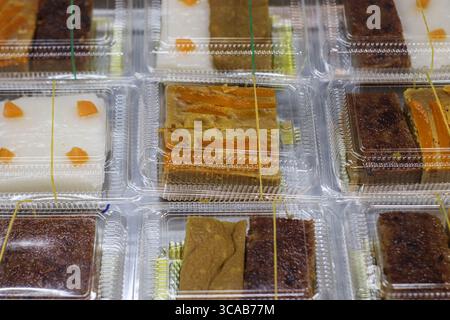 Dessert thailandesi come crema pasticcera di zucca e riso appiccicoso ordinatamente confezionati in scatole chiare in un vivace mercato notturno. Foto Stock