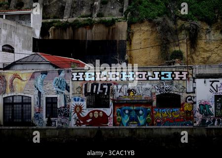 Le pareti ricoperte di graffiti a Praia das Lavadeiras ad Almada, Lisbona, aggiungono un colore audace e un carattere urbano al lungomare, contro aspre scogliere e il verde Foto Stock