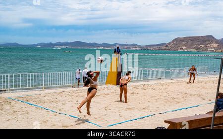 Un giocatore serve come giovani donne che giocano a pallavolo in un torneo di Beach volley lungo il Malecon (passerella sull'oceano) nel quartiere del centro. Foto Stock