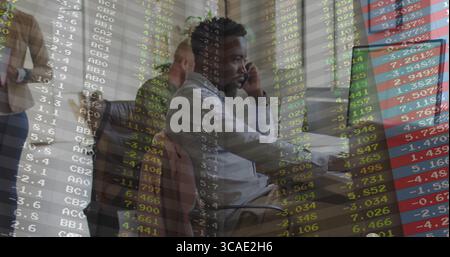 Uomo afro-americano che parla sullo smartphone con la cuffia e utilizza il computer in ufficio, dati di magazzino Foto Stock