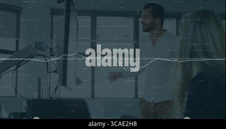 Uomo gestuale in camicia bianca che presenta su due monitor durante riunioni d'ufficio, braccio per microfono, spazio per copie Foto Stock