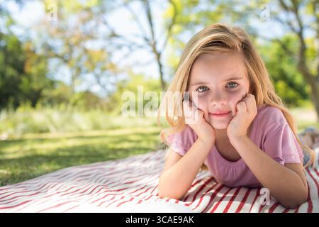 Ragazza sdraiata su una coperta da picnic a righe nel parco, con mento in mano, spazio per copiare Foto Stock
