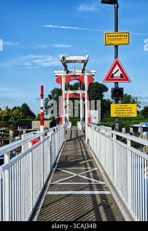 Ponte levatoio in metallo bianco con accenti rossi che si estende su un tranquillo canale in un pittoresco paesaggio olandese di polder sotto un cielo soleggiato Foto Stock