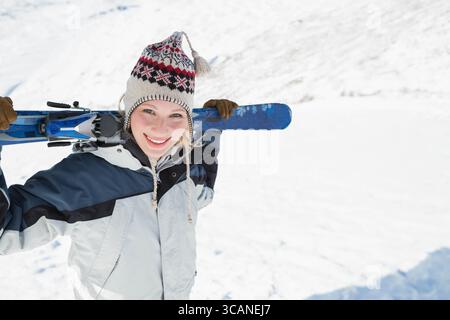 Donna in piedi su una pista innevata che indossa giacca invernale, cappello in maglia con sci blu, spazio per copiare Foto Stock
