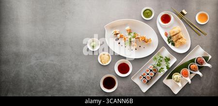 I sushi Rolls variano con riso, pesce e salse su fondo in pietra. Vista superiore con spazio di copia. Foto Stock