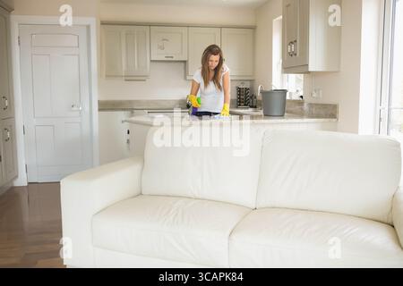 Donna che indossa guanti gialli che pulisce il piano di lavoro in granito con spugna e panno nella zona della cucina Foto Stock