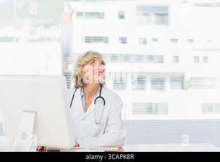 Medico donna che indossa camice da laboratorio sulla tastiera del monitor del computer con stetoscopio presso la clinica Foto Stock