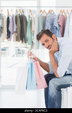Uomo seduto sulla panchina in un negozio di abbigliamento luminoso che tiene in mano borse della spesa color pastello, spazio per fotocopie Foto Stock