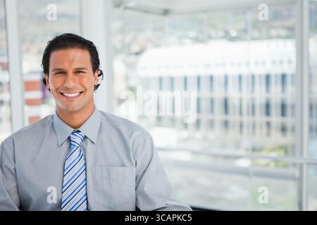 Uomo di mezza età che indossa una camicia grigia e una cravatta blu a righe sorridente alla fotocamera in ufficio, spazio per le copie Foto Stock