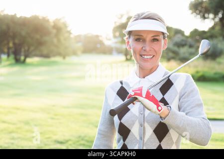 Donna di mezza età che tiene la mazza da golf sulle spalle sul fairway del golf al tramonto con visiera e guanto Foto Stock
