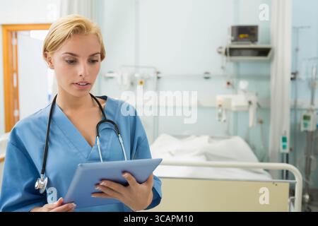 Medico donna che esamina i dati del paziente su tablet dal letto di ospedale con stetoscopio Foto Stock