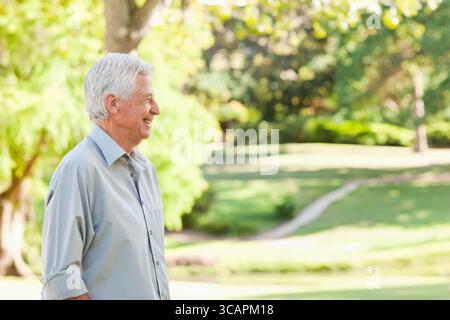 Uomo anziano in piedi nel parco, guardando attraverso la distesa erbosa, indossando una camicia con bottoni, spazio fotocopie Foto Stock