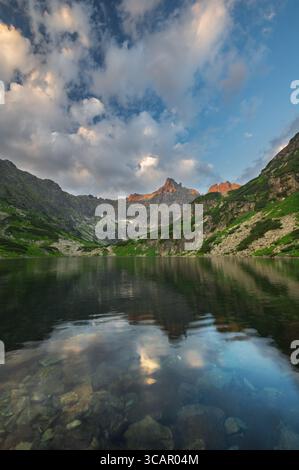 Vista delle acque tranquille che riflettono una maestosa catena montuosa sotto un cielo dipinto con morbide nuvole, abbracciando la grandezza della natura, Tatranská Javorina, Pr Foto Stock