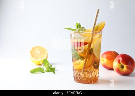 Gustoso tè freddo con limone, pesche e menta su sfondo bianco Foto Stock