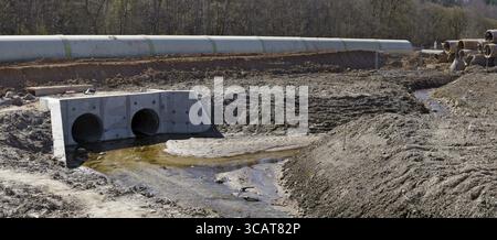 Grandi tubi fognari in calcestruzzo e cumuli di sabbia con tracce di ruote per attrezzature pesanti in un cantiere fognario nella foresta Foto Stock