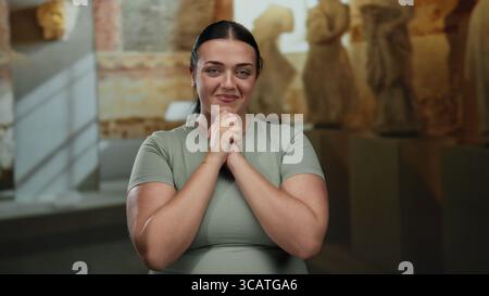 Donna sorridente e applaude nel museo moderno con sculture e luci soffuse, che mostrano gioia e apprezzamento dell'arte in un ambiente culturale al coperto. Foto Stock