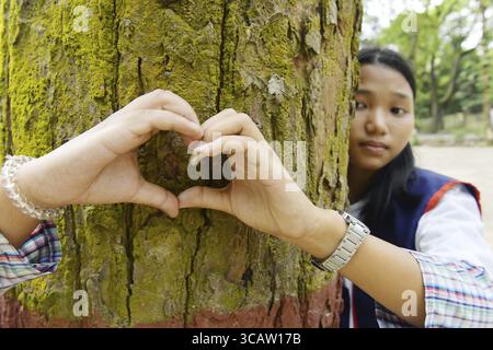 Giovane accanto ad un albero che forma con le mani una forma a cuore, riflettendo il legame con la natura Foto Stock
