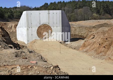 Grande raccoglitore di calcestruzzo per tubi fognari e cumuli di sabbia con tracce di ruote per attrezzature pesanti in un cantiere nella foresta Foto Stock