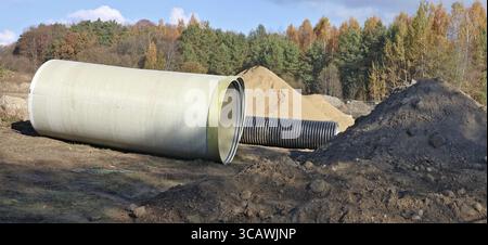 Grandi tubi fognari e un mucchio di sabbia in un cantiere forestale autunnale. Collage panoramico da diversi scatti all'aperto assolati del giorno di ottobre Foto Stock
