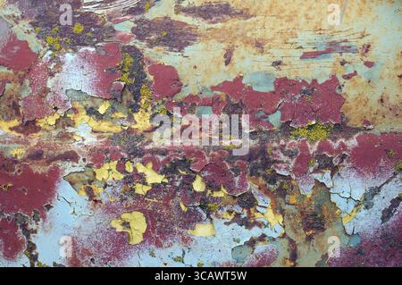 La superficie smaltata incrinata del cofano della vecchia auto era verniciata in giallo blu e rosso. Concetto di texture vintage Foto Stock