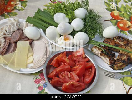 Colazione contadina su un soleggiato luglio mattina nel povero villaggio europeo. Sul tavolo - uova sode, pomodori, formaggi e lardo, verdi e pollo. Sour e Foto Stock