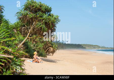 Giovane donna che si rilassa seduta sulla spiaggia di Tangalle, Sri Lanka, subcontinente indiano, Asia meridionale Foto Stock