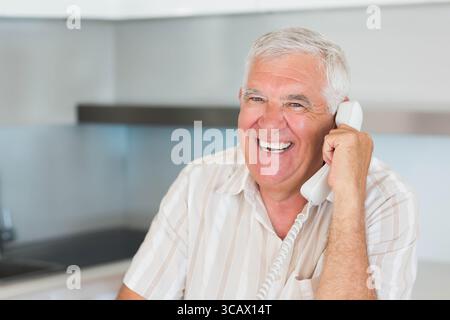 Uomo anziano che parla con un telefono cablato in una moderna cucina con ripiano e armadi, spazio per fotocopie Foto Stock