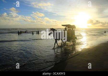 Le carrozze trainate da cavalli per il turismo passano lungo la costa della spiaggia di Parangtritis nel pomeriggio. Foto Stock