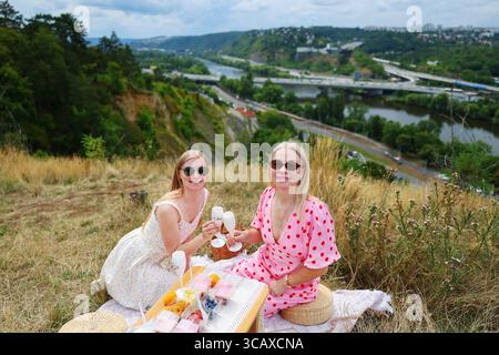 Un rilassante momento di picnic con vino e risate affacciato sul fiume e sulle verdi colline. Foto Stock