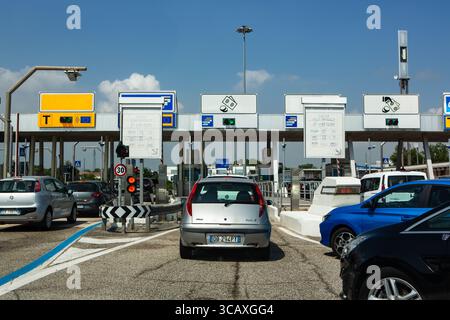 I veicoli attendono pazientemente presso un casello autostradale italiano sotto un cielo azzurro in una giornata limpida, creando un tipico scenario di viaggio su strada. Foto Stock