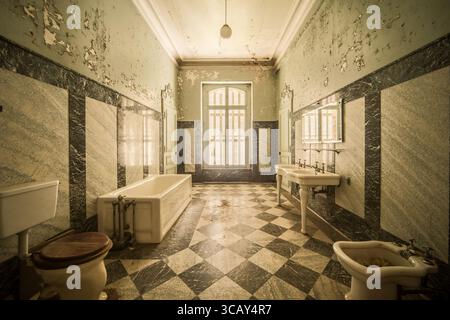 Bagno d'epoca abbandonato con vernice sbucciante, piastrelle in marmo e infissi classici a Château Lumière Foto Stock