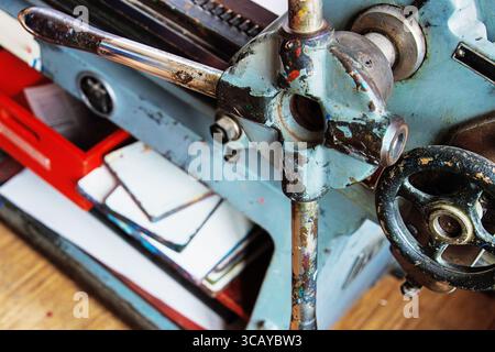 Stampa d'epoca con manovella usurata e componenti meccanici, insieme a una pila di lastre e carta inchiostrate. Foto Stock