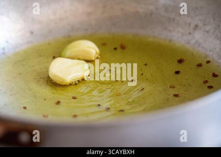 Spicchi d'aglio sfrigolanti nell'olio d'oliva e peperoncino in una padella. Un classico passo di cucina casalinga per infondere sapore all'olio Foto Stock