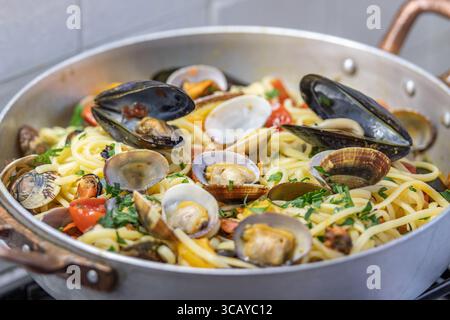 Cuocere gli spaghetti con cozze, vongole, pomodori ciliegini e prezzemolo in una teglia di acciaio inossidabile sul piano cottura in cucina Foto Stock
