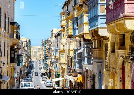 Colorate case a schiera maltese con balconi chiusi lungo Republic Street con Forst St Elmo in lontananza, la Valletta, Malta Foto Stock
